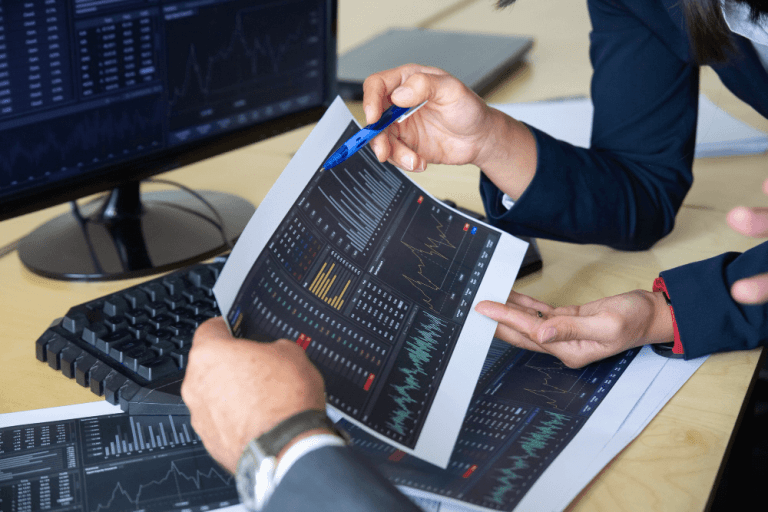 brokers discussing trading strategy holding papers with financial data pointing pen at charts cropped shot broker job or stock market exchange concept