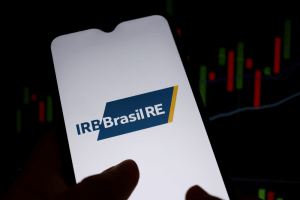 Tela de celular com logo do IRB, gráfico de ações ao fundo
