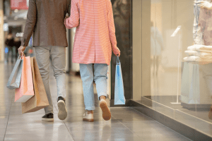 Casal andando por corredor de shopping center segurando uma sacola