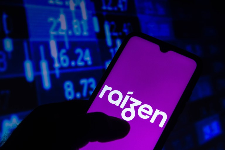 Foto de celular com logo da Raízen, ilustração de gráfico com cotações de ações ao fundo