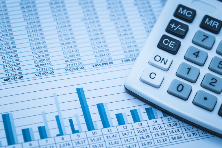 Foto de calculadora em cima de folha de balanço de uma empresa, com gráficos e números