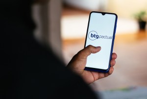 Mão segurando celular com o logotipo do BTG Pactual