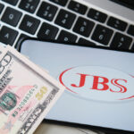 Celular com o logo da JBS e notas de dinheiro ao lado