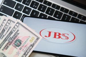 Celular com o logo da JBS e notas de dinheiro ao lado