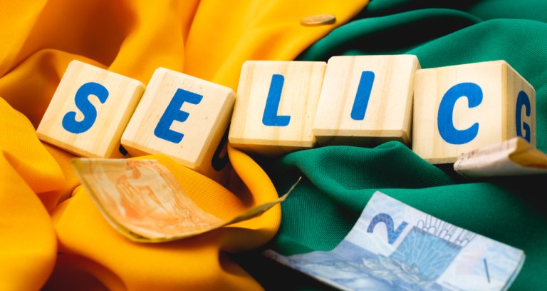 Blocos de letras formam a palavra Selic com notas de real ao redor e um fundo verde e amarelo