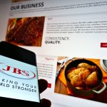 Celular com logo da JBS e site da empresa no fundo