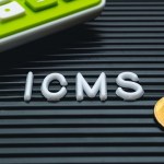 Sigla ICMS ao lado de calculadora e moeda de real.
