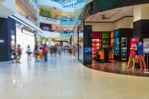 Imagem com parte borrada mostra corredor de shopping com lojas abertas
