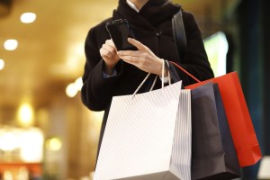 Pessoa com sacolas de compras no braço e utilizando o celular