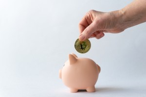 Mão colocando moeda de Bitcoin em cofre de porquinho