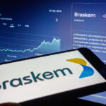 celular exibe logotipo da Braskem com tela ao fundo mostrando evolução das cotações da empresa