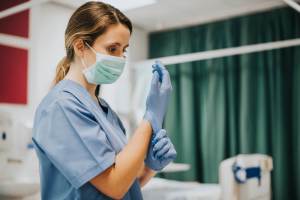 Enfermeira calçando luvas em sala de hospital