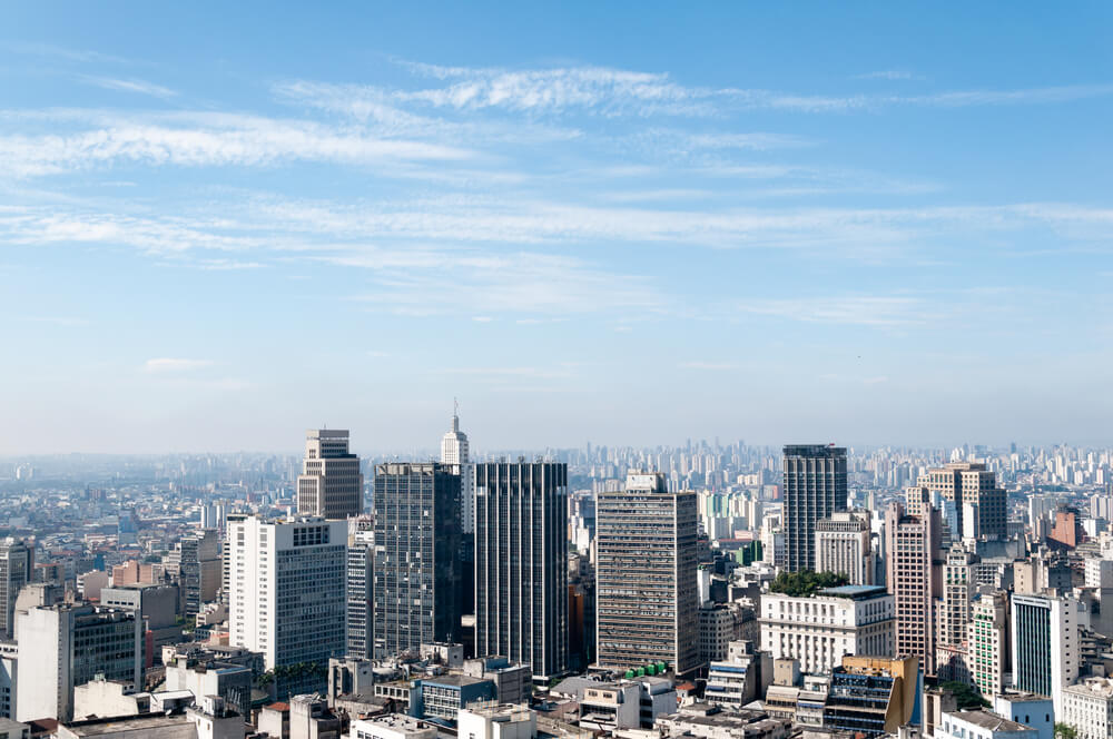 Imagem aérea da cidade de São Paulo, com prédios comerciais ao centro e construções ao fundo e redor.