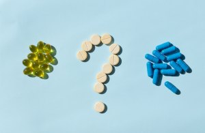 mesa com pilhas de pílulas amarelas e azuis e ponto de interrogação formado por pílulas brancas