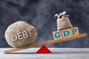 imagem mostra balança pendendo para o lado de uma pedra escrito "dívida", em inglês, enquanto do outro lado aparece uma sacola com os dizeres PIB (GDP, na sigla em inglês)