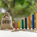 Saco com a palavra dívida escrita em inglês, ao lado de gráfico ilustrando crescimento do endividamento