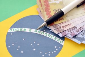 Imagem de dinheiro com caneta por cima sobre uma bandeira do Brasil