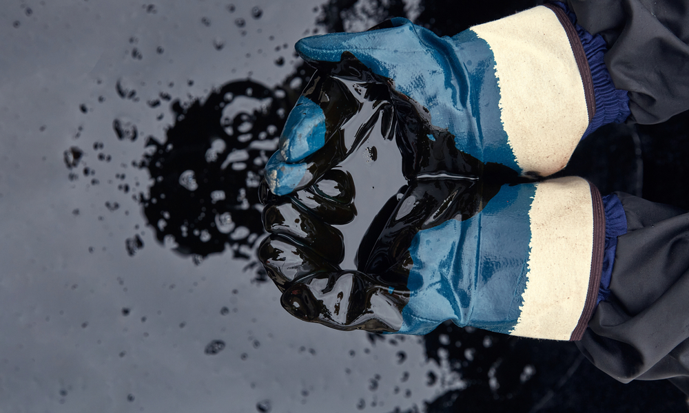 Foto de mãos com luvas mexendo em um barril de petróleo